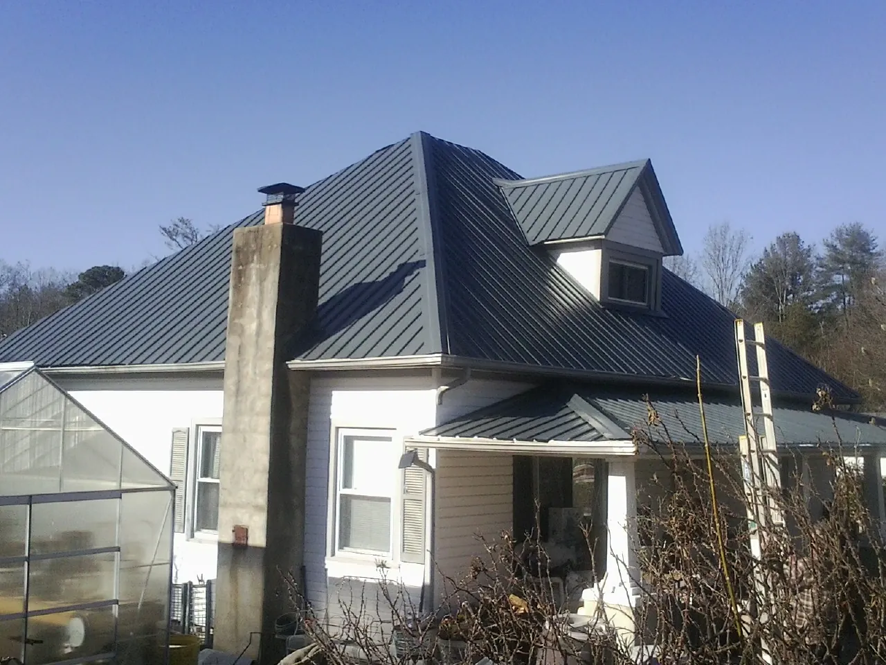 Dark blue standing seam metal roof on a white farmhouse with dormer — Slate & Tile Roof Repair by Roofing Brothers in Harwick
