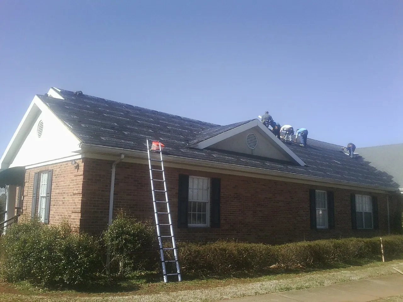 Crew tearing shingles off a brick ranch roof with a ladder set — Metal Roof Repair work by our crew in Harwick