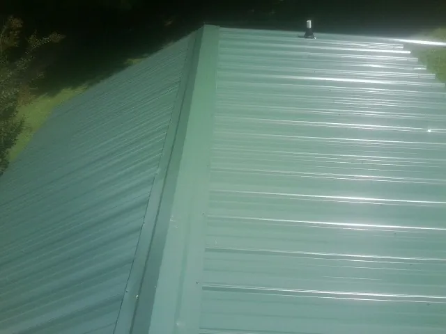 New green metal panels meeting at the ridge of a roof — Flat Roof Repair work by our crew in Harwick