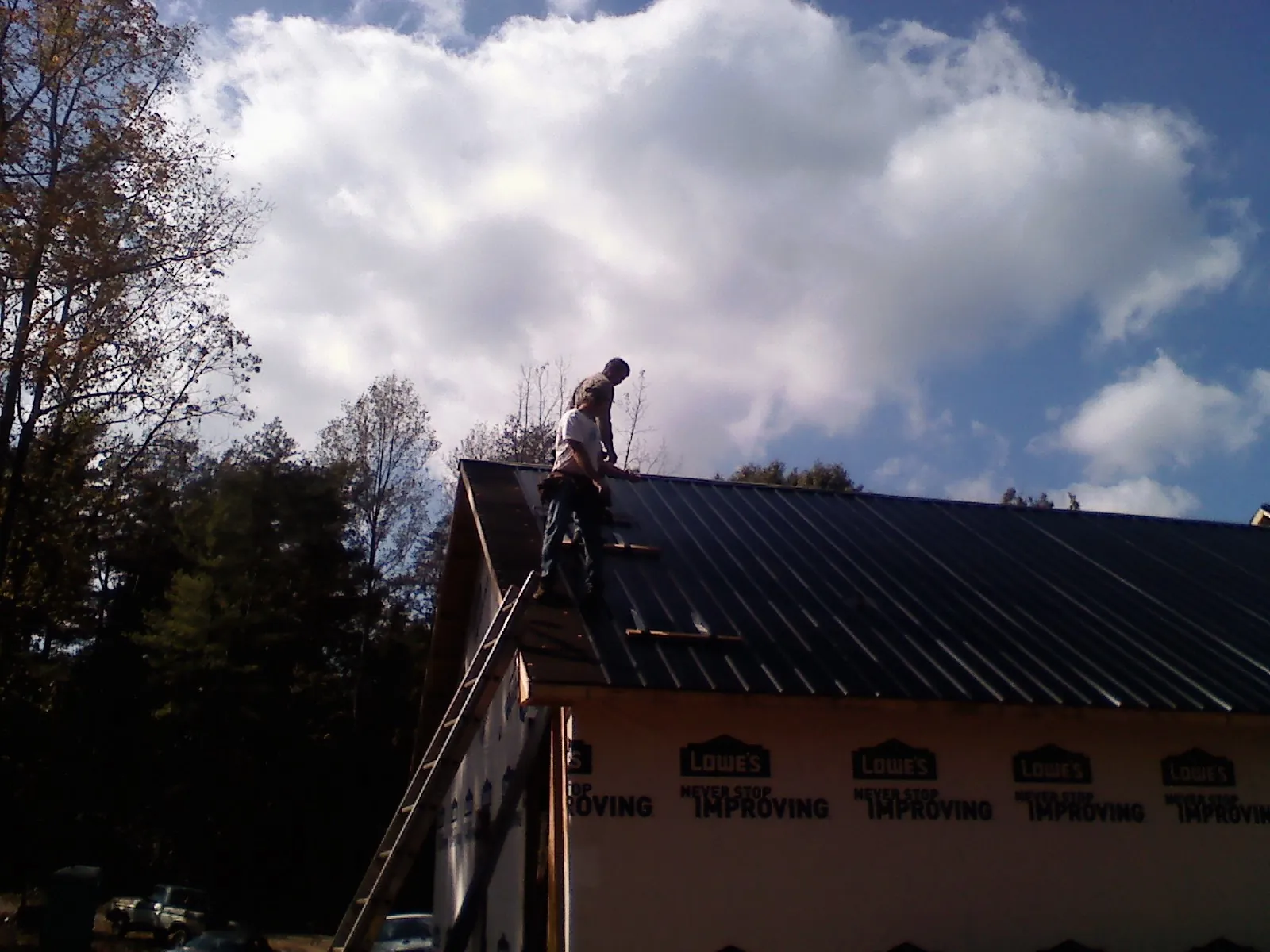 Roofer fastening dark metal panels high against a cloudy sky, from a Roof Inspection job in Harwick