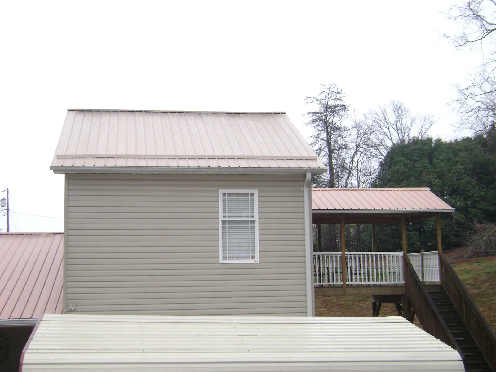 Tan metal roofs on a two story addition and attached porch, from a Roof Replacement job in Harwick
