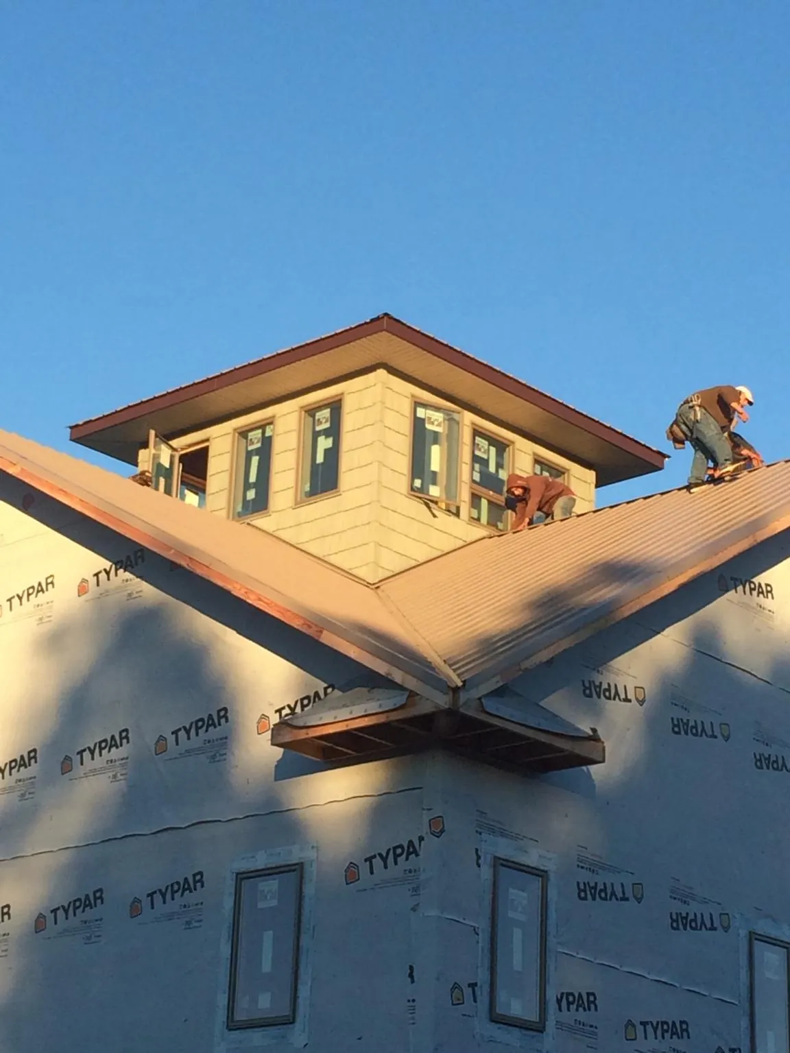 Roofers working around a rooftop cupola on a new metal roof at sunset — Roof Waterproofing in Harwick by Roofing Brothers